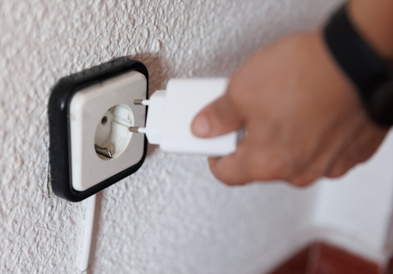 Foto de archivo de una persona sujetando un cargador frente a un enchufe