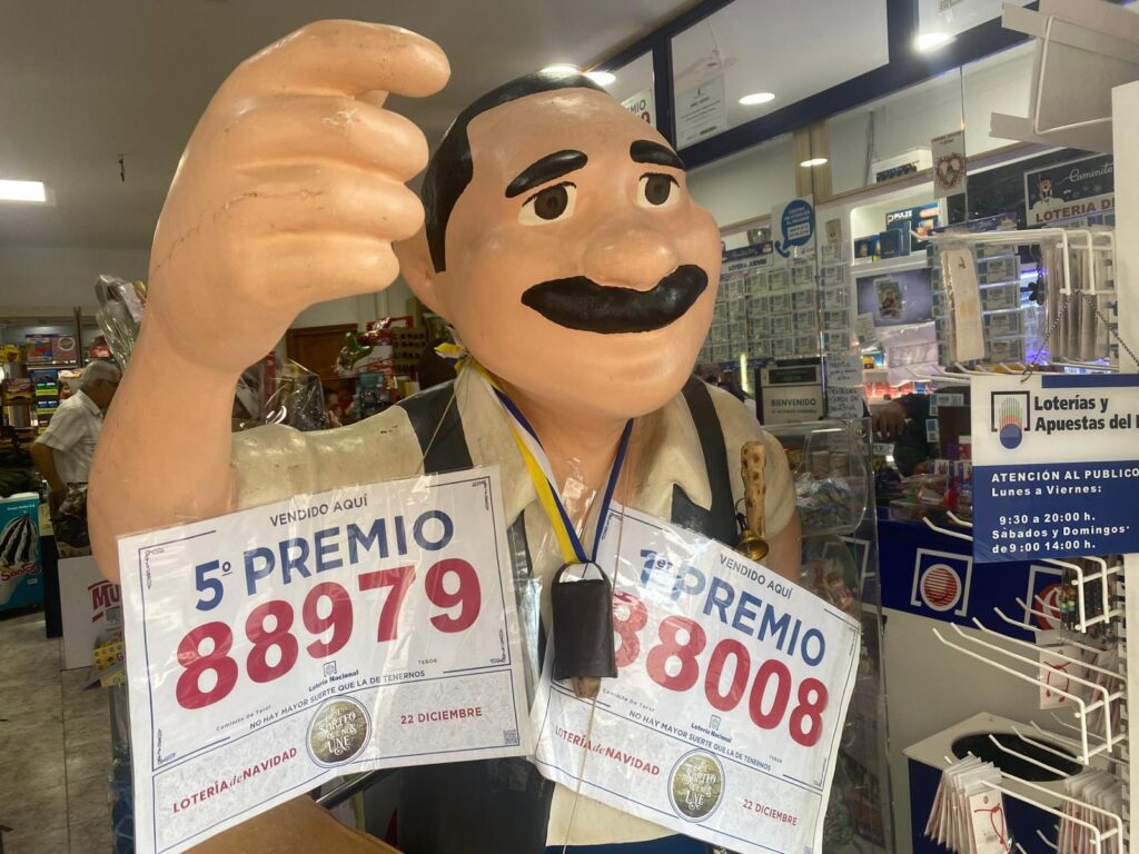 Una de las tradiciones en la administración de Lotería de Caminito de Teror en Gran Canaria es que quién compra un número lo pase por el cencerro que cuelga de su escultura / RTVC / Estefanía de Blasio