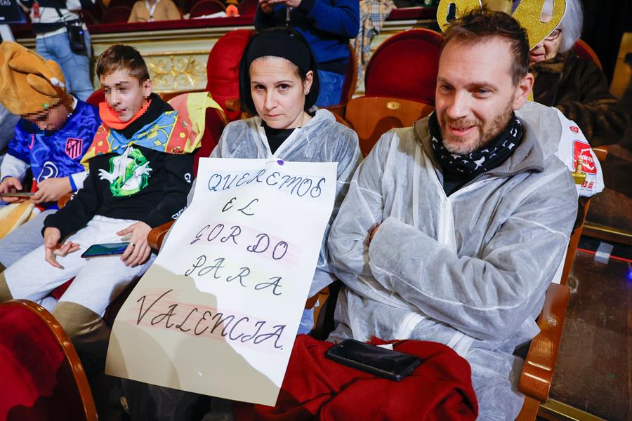 Dos asistentes al tradicional sorteo de la Lotería de Navidad que se celebra este domingo en el Teatro Real, en Madrid, con batas de voluntarios que han colaborado en labores de limpieza y reconstrucción de las zonas afectadas por la dana en Valencia. EFE/Javier Lizón