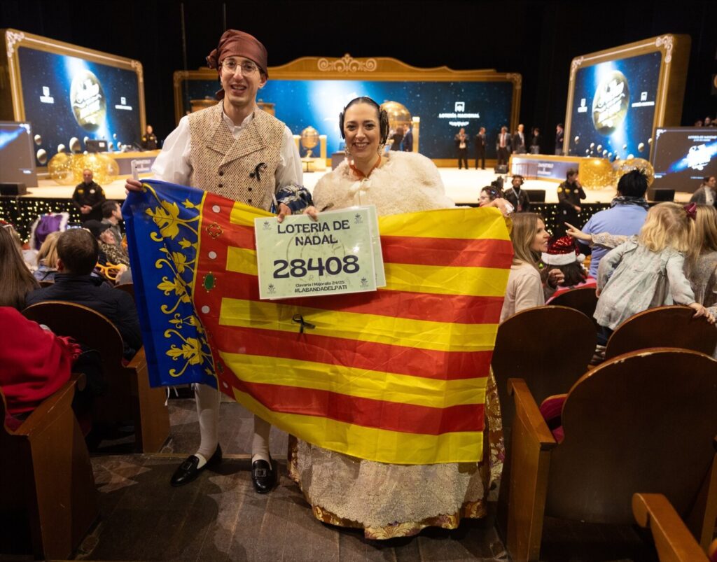 Una pareja vestidos con el traje de fallera y una bandera de la Comunidad Valenciana durante la celebración del Sorteo Extraordinario de la Lotería de Navidad 2024, en el Teatro Real, a 22 de diciembre de 2024, en Madrid (España) / Eduardo Parra / Europa Press 