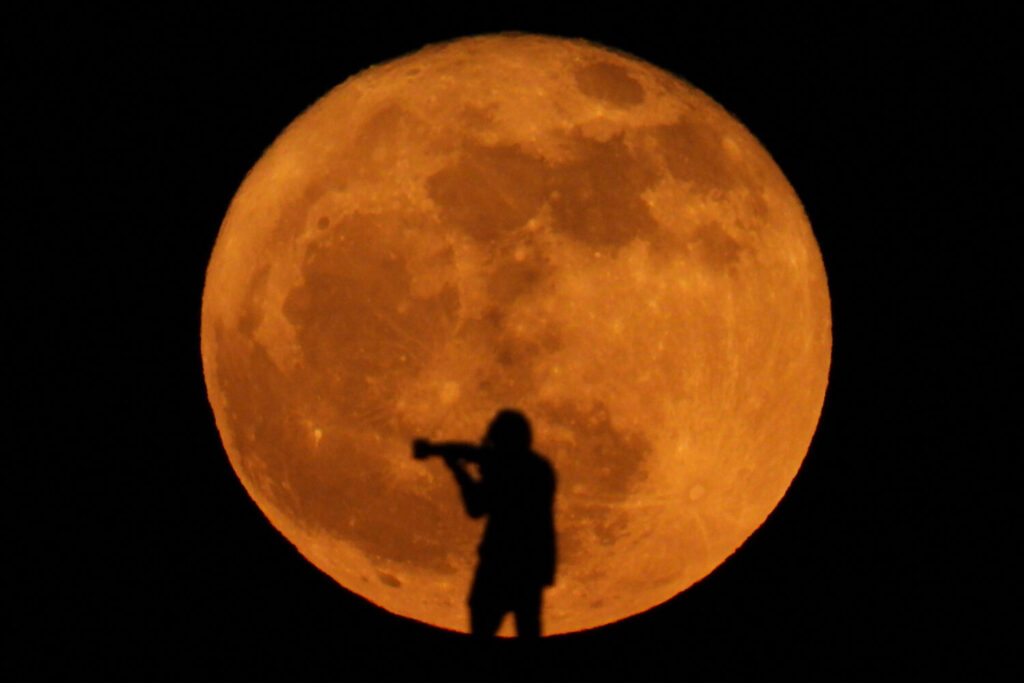 Un fotógrafo se siluetea contra la luna llena conocida como luna de fresa en Arinaga, Gran Canaria, 11 de junio de 2025. REUTERS/Borja Suárez