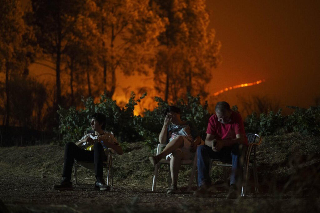 Una familia en el exterior de su vivienda, que ha quedado rodeada por el fuego, en el incendio forestal de A Rúa, en Ourense.