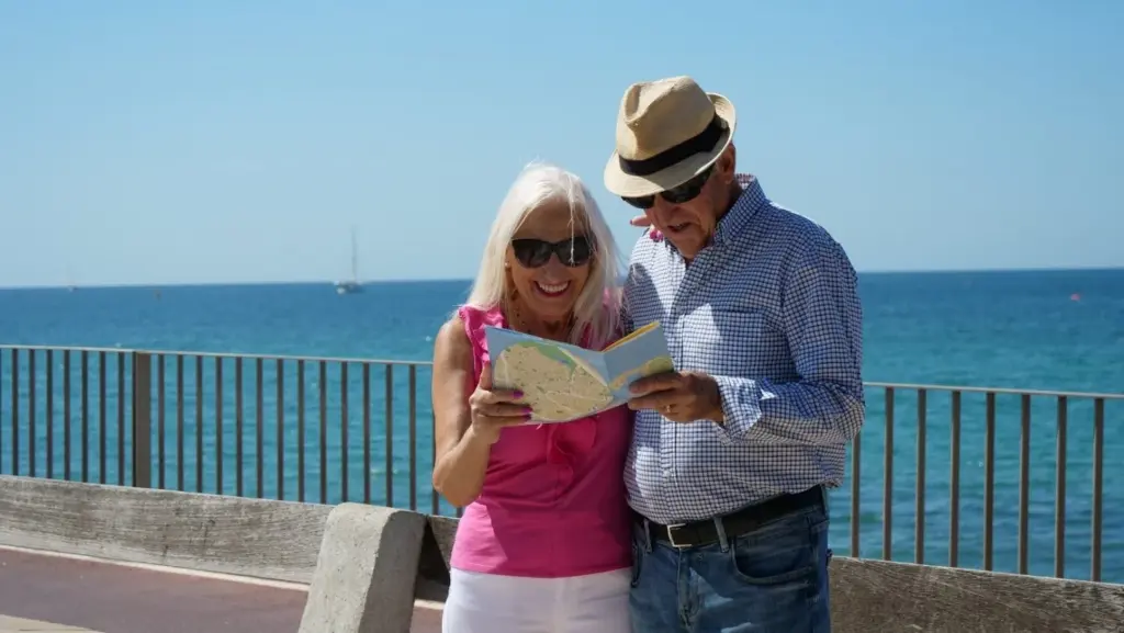 Dos personas mayores leen un mapa en la costa | Imserso