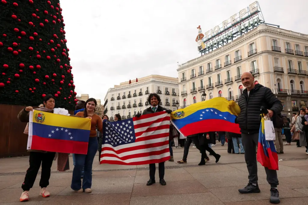 La gente sostiene banderas estadounidenses y venezolanas, mientras reaccionan a las noticias después de que el presidente de Estados Unidos, Donald Trump, dijera que Estados Unidos atacó a Venezuela y capturó a su presidente Nicolás Maduro, en Madrid, España, el 3 de enero de 2026. REUTERS/Violeta Santos Moura