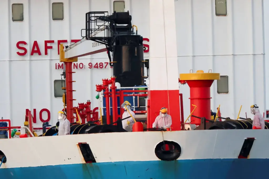 Trabajadores con equipos de protección individual (EPI) permanecen a bordo de un buque cisterna junto al crucero MV Hondius, afectado por un brote de hantavirus, en el puerto de Granadilla de Abona, en Tenerife, España, el 11 de mayo de 2026. REUTERS/Hannah McKay