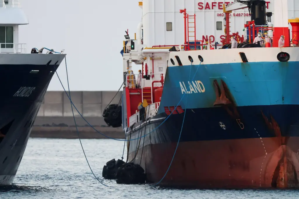 Trabajadores con equipos de protección individual (EPI) permanecen a bordo de un buque cisterna junto al crucero MV Hondius, afectado por un brote de hantavirus, en el puerto de Granadilla de Abona, en Tenerife, España, el 11 de mayo de 2026. REUTERS/Hannah McKay