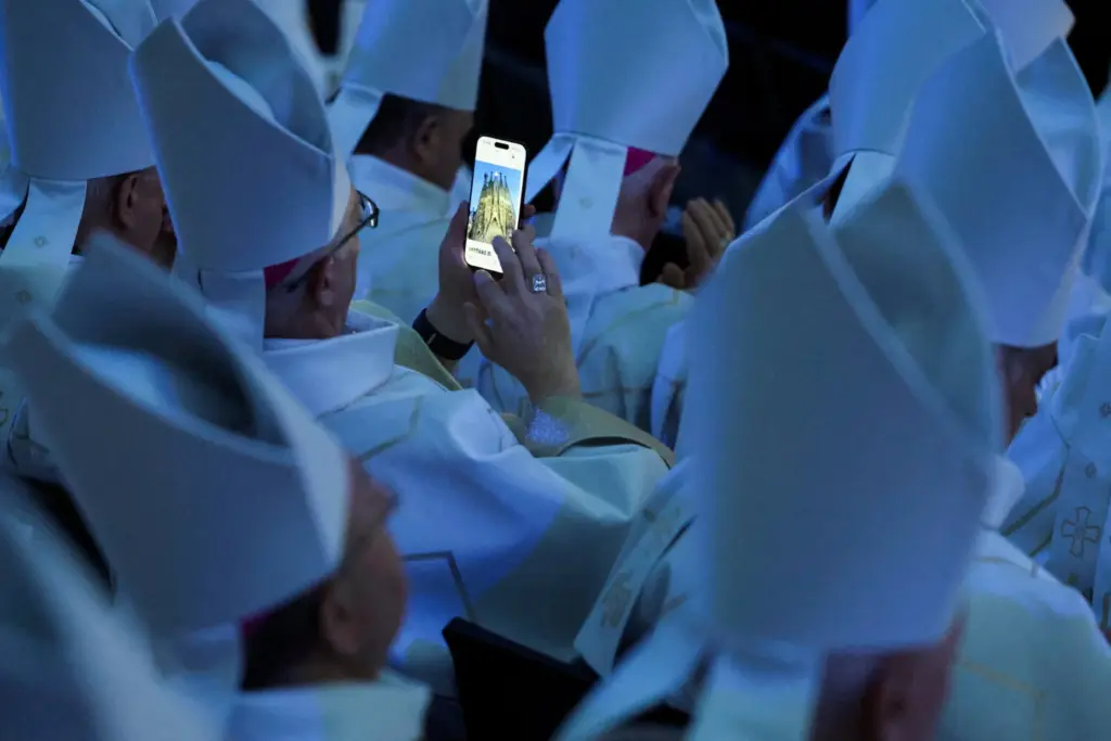 Un miembro del clero mira fotografías de la Basílica de la Sagrada Familia en un teléfono inteligente el día de la inauguración y bendición de la Torre de Jesucristo