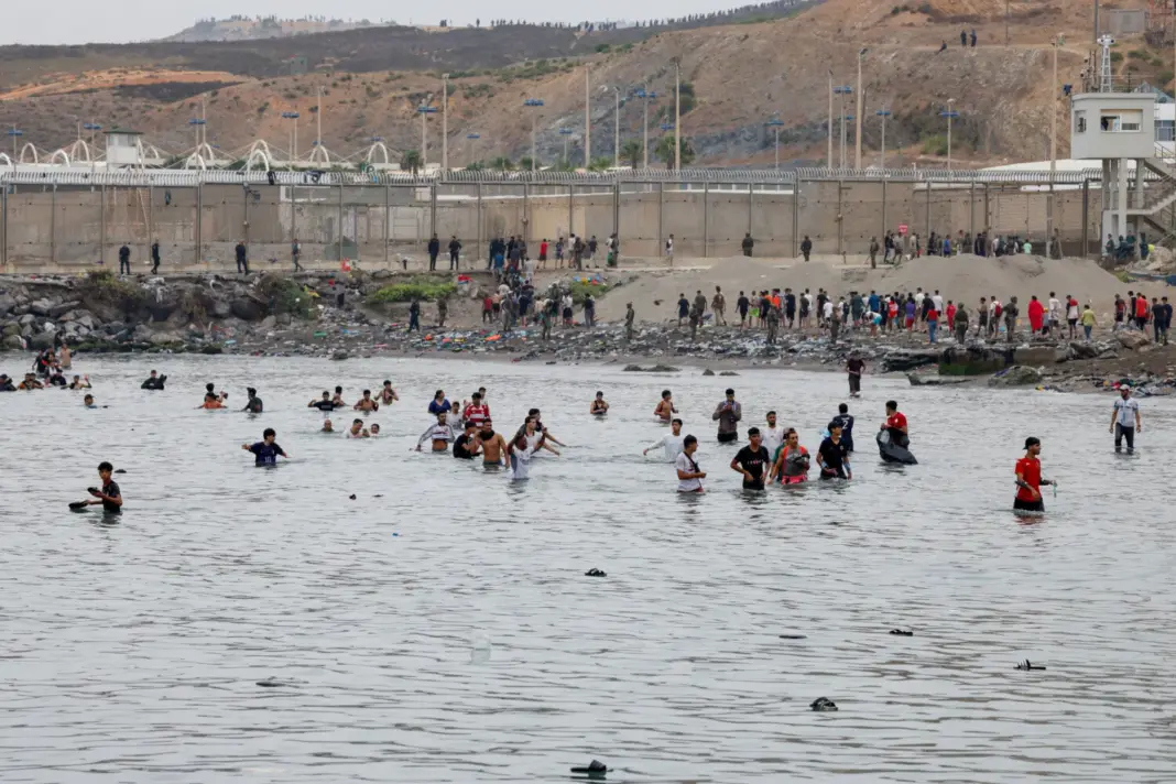 Personas avanzan con dificultad por el agua para entrar en España y, al fondo, otras que acaban de entrar regresan a Marruecos, en medio de cruces masivos de migrantes a pie y por mar desde Marruecos hacia territorio español, en Ceuta (España), el 31 de julio de 2026. REUTERS/Jon Nazca
