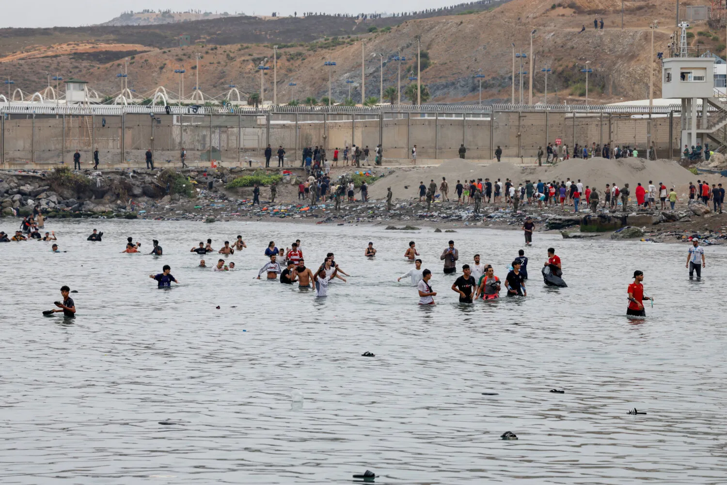 Personas avanzan con dificultad por el agua para entrar en España y, al fondo, otras que acaban de entrar regresan a Marruecos, en medio de cruces masivos de migrantes a pie y por mar desde Marruecos hacia territorio español, en Ceuta (España), el 31 de julio de 2026. REUTERS/Jon Nazca
