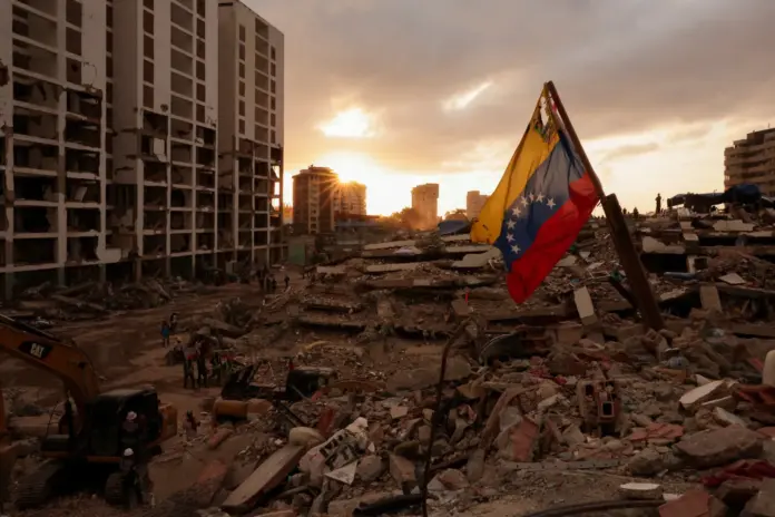 Una bandera de Venezuela ondea mientras la gente busca los cuerpos de sus seres queridos entre los escombros, tras los terremotos que sacudieron Venezuela el 24 de junio —causando la muerte y el desplazamiento de miles de personas—, en Caraballeda, La Guaira, Venezuela / REUTERS/Gaby Oraa